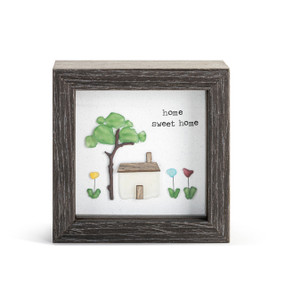 A gray wood shadow box with a pebble art inside of a house, tree and flowers that says "home sweet home".