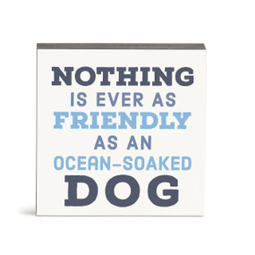 A small square white wall art with the saying "Nothing is ever as friendly as an ocean-soaked dog".