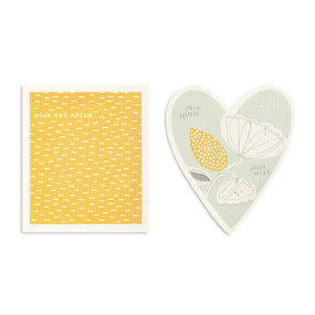 Two yellow and gray biodegradable dish cloths. One is heart shaped with an illustrated flower and the other is yellow with the saying "rise and shine".