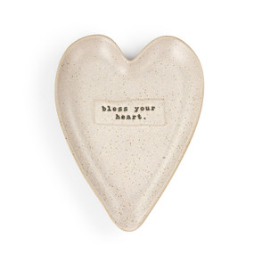 A pale pink speckled heart shaped ceramic spoon rest with the saying "bless your heart" on it.