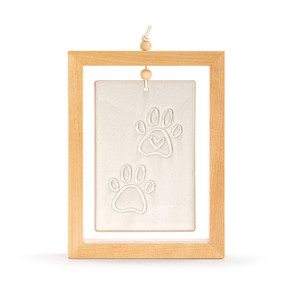 A cream ceramic plaque with an image of two paw prints suspended inside a light wood open frame.