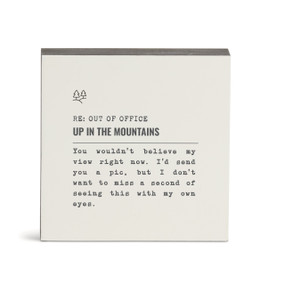 A white square wall art with the saying "RE: Out of Office Up in the Mountains" with a short write up about someone in the mountains.