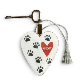 A heart shaped white sculpture with illustrated black paw prints with a silver tassel and metal key attached. The heart has the saying "Furever" inside a red heart.