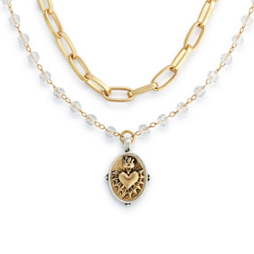 Detail view of the charm on a gold chain and beaded necklace with a gold sacred heart charm with a silver border.