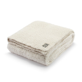 A sand and cream blanket with a tag that says "Kindness" displayed folded.