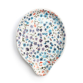 Top down view of a cream ceramic spoon rest with small flowers all over it primarily in blue and purple.
