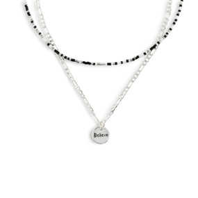 A layered necklace made up of a silver chain with a round silver charm that says "Believe" and a layer of black, gray and white small beads.