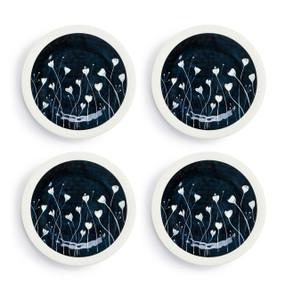 A set of four white melamine appetizer plates with dark blue in the middle and small white flowers, displayed set out next to each other.