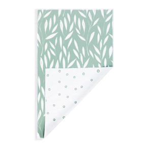 A rectangular double sided towel. One side is white with small green circles and the other is green with a white leaf pattern, displayed with the white corner turned back.