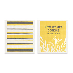 Two yellow and gray biodegradable dish cloths. One is yellow and gray stripes and the other is yellow with leaf illustrations and the saying "Now we are cooking (& cleaning)".