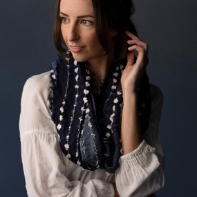 A dark blue textured infinity scarf with white strings running through it and a short fringed edge, being worn by a woman in a white blouse.