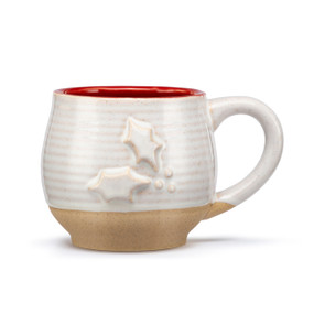 A cream ceramic mug with a tan textured base and red interior. The mug has a raised holly leaf on the front.