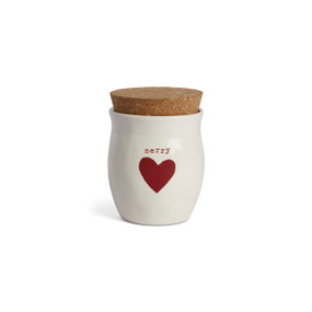 A cream ceramic container that says "merry" with a red heart and a cork lid. There is a poured candle inside.