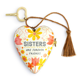 A heart shaped musical sculpture in a yellow and orange floral pattern that reads "Sisters Are Forever Friends". The heart has a bronze tassel and gold key attached.