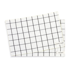 A set of two cream fabric placemats with a black plaid pattern. Each has a small fabric tag in the bottom right corner that says "Gather 'Round" and "Be Happy".