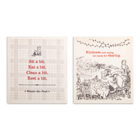 Two cream biodegradable dish clothes. One says "Sit a bit. Eat a bit. Clean a bit. Rest a bit." and the other has an image of Pooh and friends eating and says "Kindness and caring are made for sharing".