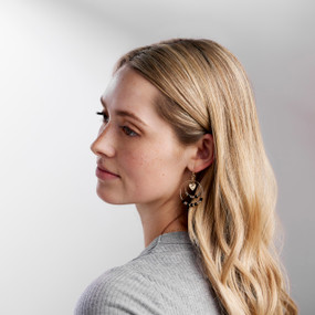 A blond woman looking back over her shoulder and wearing a pair of gold dangling earring with small beads and a heart.