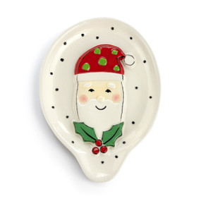 A white stoneware spoon rest with black dots and a raised Santa face with holly.