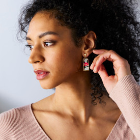 A woman wearing a pair of hanging rectangular earrings with artwork of a camellia tsubaki flower.