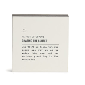 A white square wall art with the saying "RE: Out of Office Chasing the Sunset" with a short write up about someone watching the sunset in the mountains.