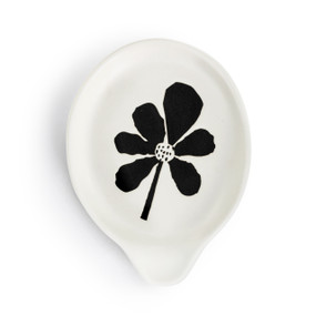 A white ceramic spoon rest with a bold black flower in the center.