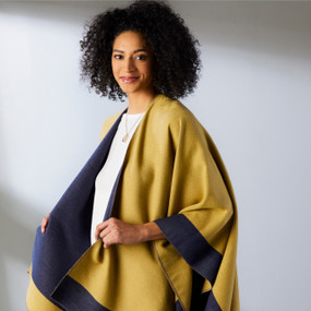 A woman wearing a reversible navy blue and mustard colored wrap with the mustard color on the outside.