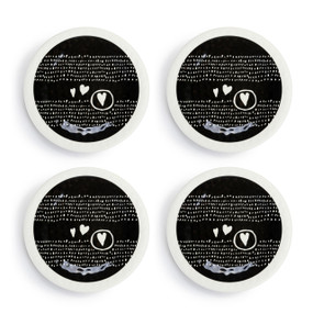 A set of four white melamine appetizer plates with a black middle that has white dots and hearts, displayed set out next to each other.