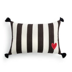 A black and white vertical striped rectangular pillow. There is an applique red heart in the corner and black tassels on each corner.