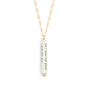 A gold chain necklace with a white scroll charm. The scroll has the scripture verse from Jeremiah 29:11.