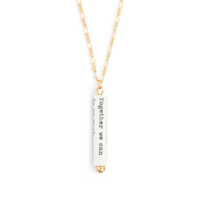 A gold chain necklace with a white scroll charm. The scroll has a saying from Helen Keller.