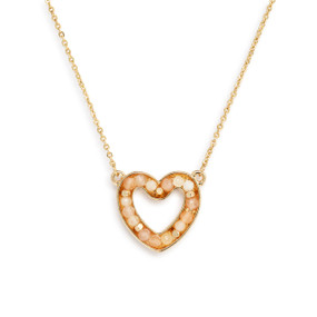 Detail view of the charm on a gold chain necklace with a heart shaped charm filled with small cream stones.