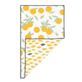 A rectangular double sided towel. One side is white with illustrated oranges and the other is white with an illustrated leaf pattern, displayed with the leaf corner turned back.