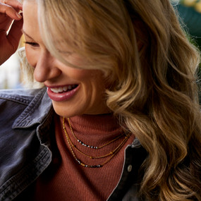 A woman wearing a necklace made of three different strands of beads with gold chains.
