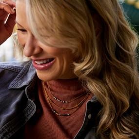 A woman wearing a necklace made of three different strands of beads with gold chains.