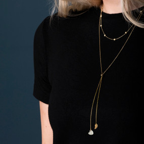 Close up of a woman wearing a black top and a long gold chain lariat necklace with a silver heart and gold wing charms at the bottom.
