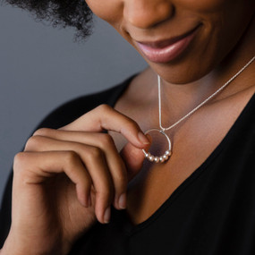 A woman holding the silver ring with beads on a becalm necklace that she is wearing.