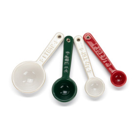A set of four ceramic measuring spoons in white, green and red with the measurements on the handles.
