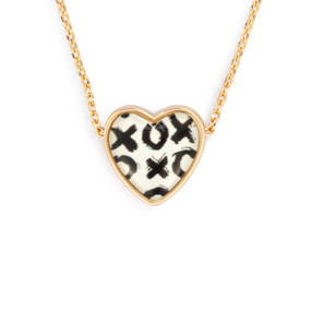 Detail view of the charm on an adjustable gold chain necklace with a heart shaped charm of black x's and o's on a white background.