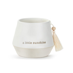 A small round white ceramic cachepot with "a little sunshine" on the front with a cream tassel.