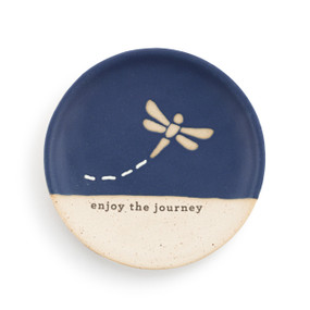 A small round blue and tan ceramic trinket dish. The blue is on the top half with a dragonfly and the saying "enjoy the journey" in the bottom half.