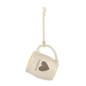 A cream ceramic mini mug that says "grateful" with the image of a heart on the front, shown hanging with a coffee pod inside.