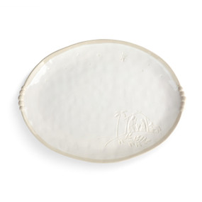 An oval cream ceramic platter that has the image of the Nativity in the bottom right corner and decorative elements on the sides.
