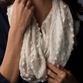 A white textured infinity scarf with a short fringed edge, being worn by a woman in a dark blue blouse.