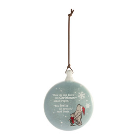 A round disc ornament with the image of Pooh and Piglet standing in snow and the saying "How do you know it's Christmas?' asked Piglet. "You feel it all around," said Pooh.
