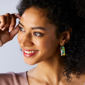 A woman wearing a pair of earrings with a vertical rectangle of abstract florals on red.