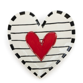 A white heart shaped plate with black stripes and a raised red heart in the center.