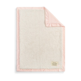 A plush cream blanket with a light pink edge and back. There is a fabric patch in the bottom right corner.