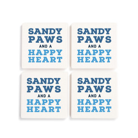 A set of four white ceramic coasters with the saying "Sandy Paws and a Happy Heart".