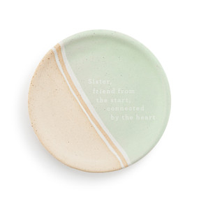 A small tan and light green round ceramic trinket dish with the saying "Sister, friend from the start, connected by the heart" in the middle.
