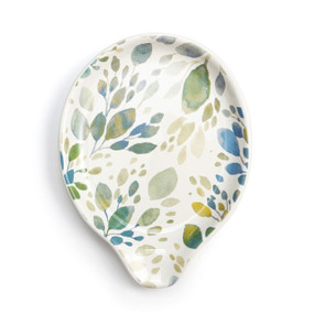 Top down view of a cream ceramic spoon rest with a drawing of leaves in shades of green and blue.